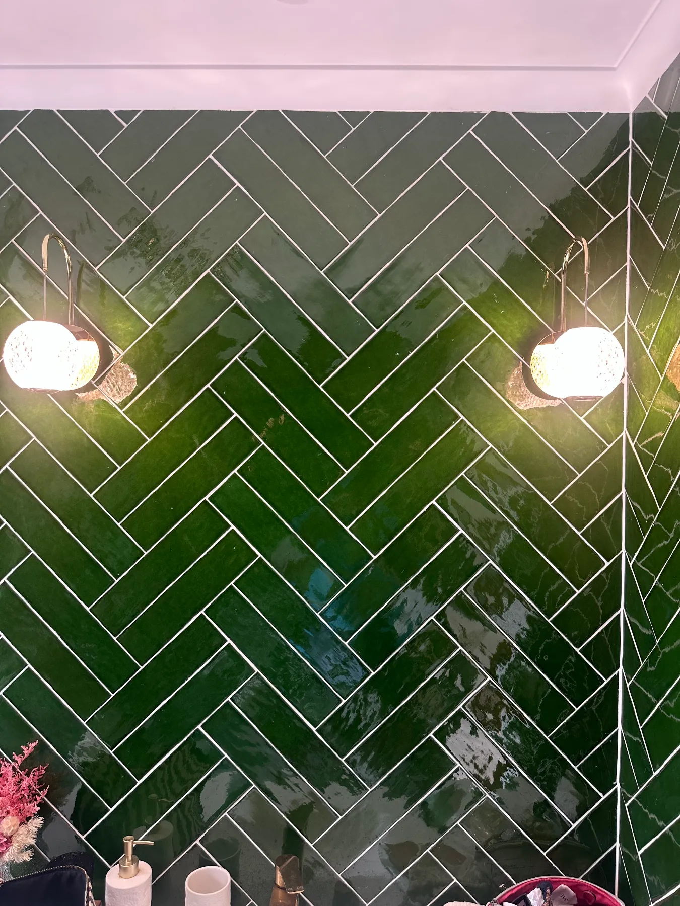Wall lights beside a bathroom mirror above green tiles