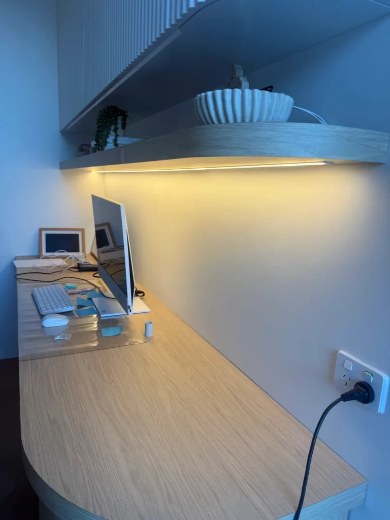 Home desk lit by LED strip lighting along an overhead shelf