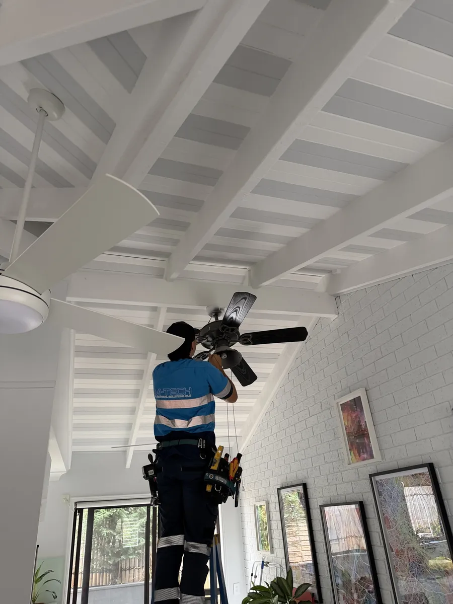 M-Tech electrician working on a ceiling fan under a raked, beamed ceiling in a Springwood home