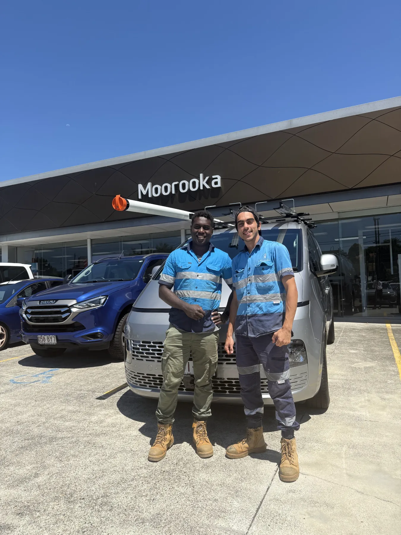 M-Tech electricians in blue branded shirts beside their work van in Brisbane